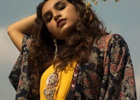 A fashionable South Asian woman with flowers poses stylishly under a blue sky.