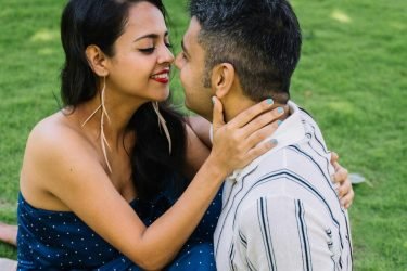 Loving couple sitting close on a picnic blanket, sharing a joyful moment outdoors.